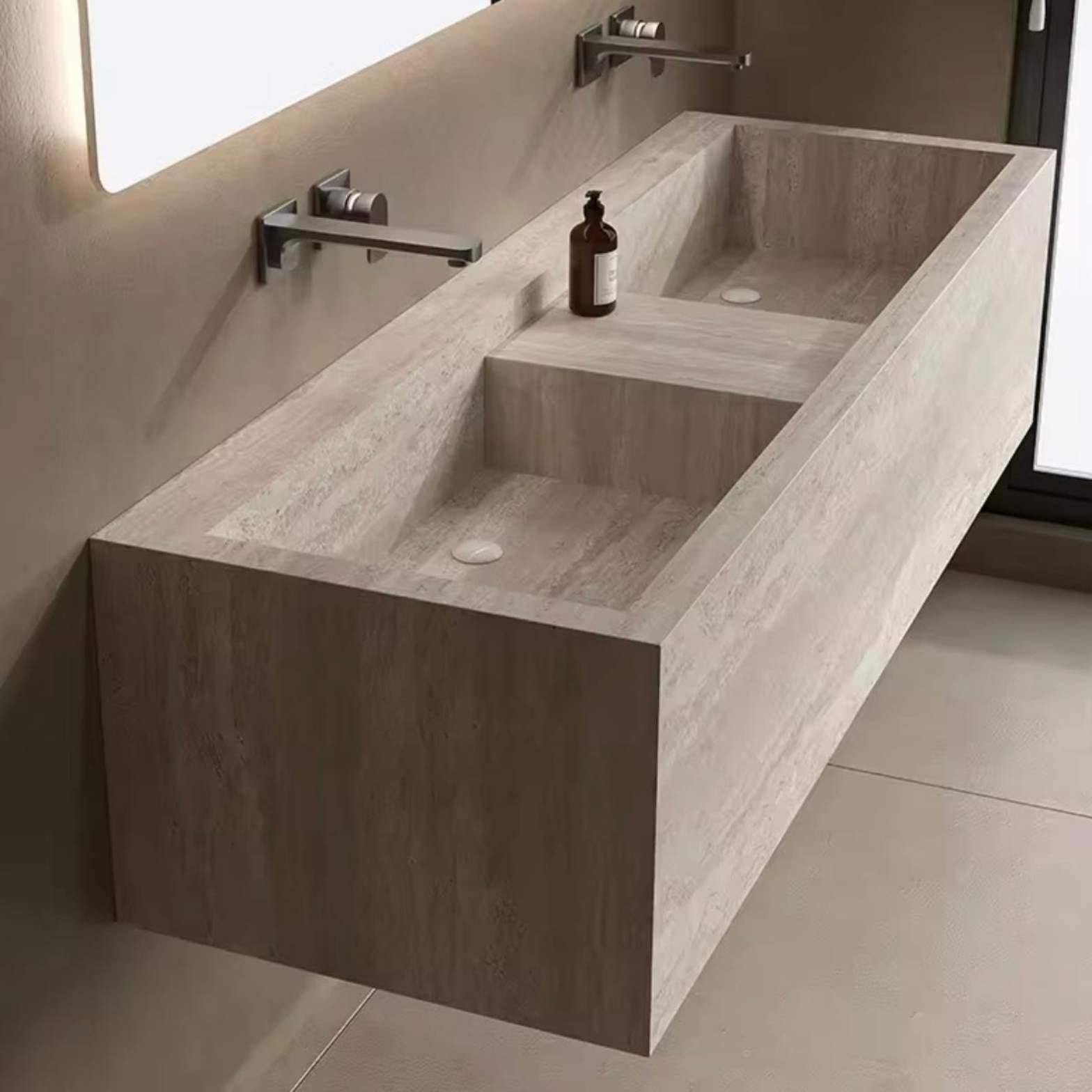 A long, floating bathroom vanity crafted from beige travertine stone with two built-in square sinks and sleek silver wall-mounted faucets.
